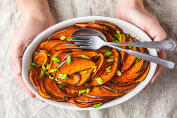 Baked sliced sweet potato with green onions in hands.