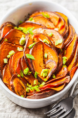 Baked sliced sweet potato with green onions in white dish.