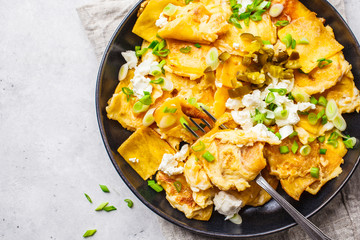 Mexican tortilla egg migas with feta and green onions in a black plate on white background, top view.