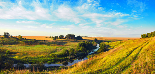 Sunny summer panoramic landscape with ground country road,river,golden wheat fields and green meadows 