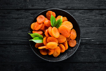 Dried apricots in a bowl on a black background. Top view. Free space for your text.