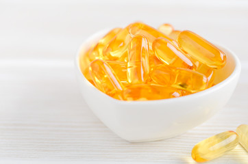 Fish oil capsules on a white wooden background, vitamin D supplement, selective focus.