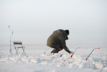 Winter fishing. Focus on the fishing rod. Fisherman in the background