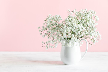 Home interior floral decor, white gypsophila flowers. Elegant floral soft pink composition. Beautiful flowers in vase on pastel pink wall background