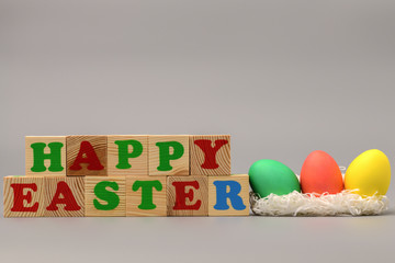 Three Easter colored eggs lie in the nest, next to the wooden cubes with the word happy on a gray background. happy Easter. Horizontal photography