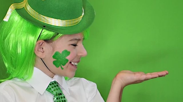 Saint Patrick celebrations over green background. I am a smiling boy with a piece of clover on my cheek holding a subject in my hand. Copy space