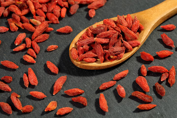 Extreme close up of dried organic goji berry fruits (wolfberries) in a wooden spoon on a black...