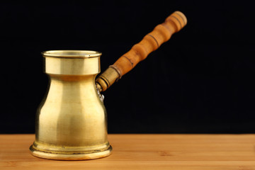 Old, vintage brass turkish coffee pot (dzhezve) with carved wooden handle on a wooden table against black background. Space for text