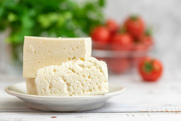 Large pieces of feta cheese in white plate and cherry tomatoes on light background. Selective focus, High key