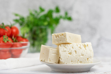 Large pieces of feta cheese in white plate and cherry tomatoes on light background. Selective focus, High key