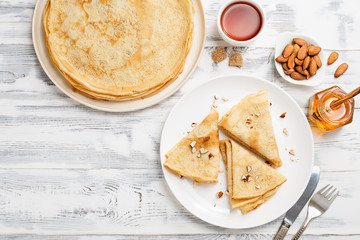 Crepes, thin pancakes with honey and nuts on a white plate . Wooden background .