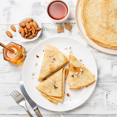 Crepes, thin pancakes with honey and nuts on a white plate . Wooden background .