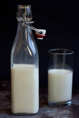 Full glass bottle of milk beside tall cup on wooden surface with copy space over dark background SELECTIVE FOCUS