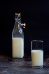 Full glass bottle of milk beside tall cup on wooden surface with copy space over dark background SELECTIVE FOCUS