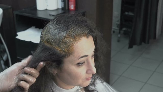 Hairdresser-stylist puts paint on individual strands of hair girl who sits in front of a mirror in the salon-beauty. Hair care. Close up. The view from the top. 4K. 25 fps.