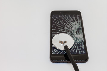 stethoscope is leaning against the screen of a black smartphone with broken glass