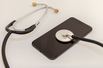 stethoscope is leaning against the screen of a black smartphone