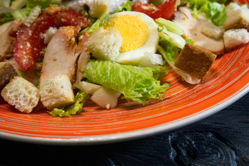 Caesar salad in red plate. Caesar salad consists of roasted chicken breast, iceberg lettuce, tomato. Popular dish of European cuisine and cuisines of other countries of world.