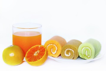 A glass of orange juice with fresh orange and Three pieces of Fancy cream rolls;orange roll coffee roll and pandon cream roll on white ceramic dish on blurred background