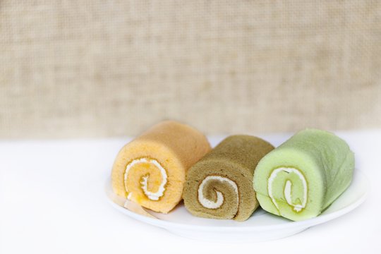 Three pieces of Fancy cream rolls;orange roll coffee roll and pandon cream roll on white ceramic dish on blurred background 