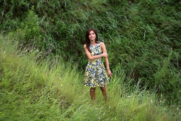 summer walk on a green ravine, a young slim pretty girl with long brown hair in a yellow dress sundress, enjoys life on the field with summer flowers