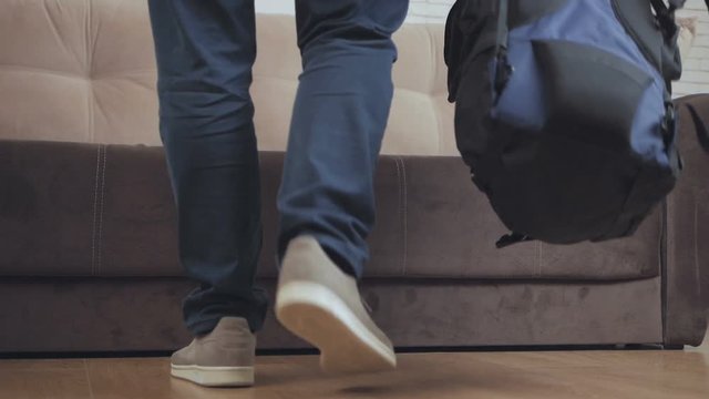 A man with a tourist backpack comes into the hotel room and puts the backpack next to the sofa. The average plan, in the frame only the feet of a person.