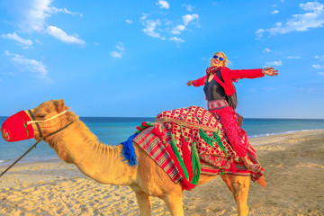 Inland sea is a major tourist destination for Qatar. Freedom woman riding camel on beach at Khor al...