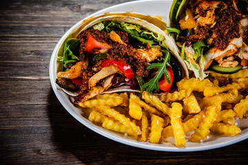 Kebab - grilled meat with french fries and vegetables on wooden background