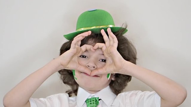 Child Celebrating St. Patrick's Day Showing his Make-up. A small, curvy boy leaf of clover and Irish flag on his cheeks showing a gesture of love. slow motion. light background