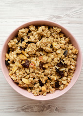 Top view, fruit granola in pink bowl over white wooden background. Flat lay, from above, overhead.