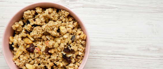 Overhead view, fruit granola in pink bowl over white wooden surface. Flat lay, from above, top view. Space for text.