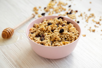 Pink bowl of fruit granola and honey over white wooden surface, low angle view. Close-up.