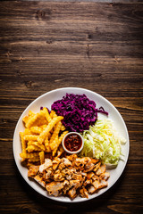 Kebab - grilled meat with french fries and vegetables on wooden background