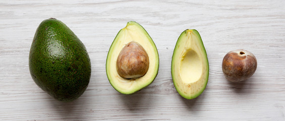 Whole and chopped avocados on white wooden surface, view from above. Top view, overhead, flat lay.