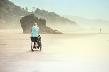 Father pushing disabled child in wheelchair along foggy beach