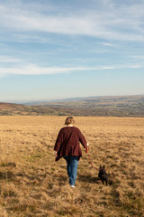 Mature woman and terrier dog walking through a meadow