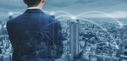 Businessman in blue suit looking at city with network connection in the city. Business network technology, logistics and blockchain business