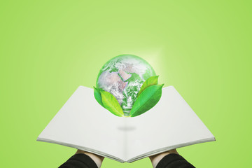 Hand holding opened book with globe with leaves, on green background. Element of this image are furnished by NASA