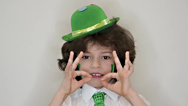 Child Celebrating St. Patrick's Day Showing his Make-up. A small, curvy boy with leaf of clover and Irish flag on his cheeks showing a gesture okay. slow motion. green background