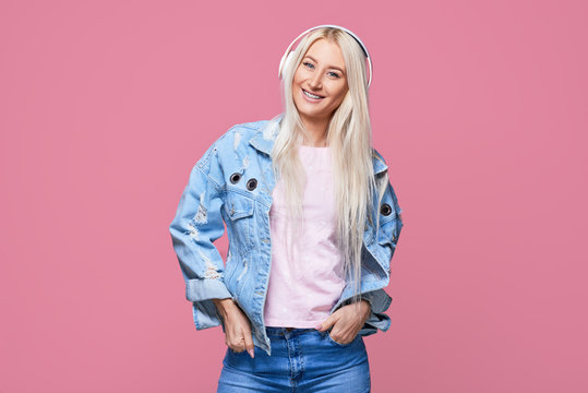 Dentistry and health concept. Pretty young blond woman with broad shining smile wears braces on teeth, poses alone against pink background. Listening to music in headphones with pleasure