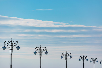 Street lanterns on against shine blue sky with clouds