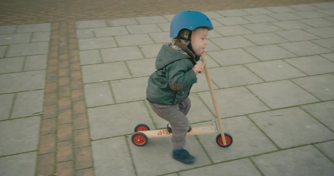 Little toddler riding his scooter in a town square