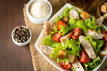 Fresh salad made of tomato, ruccola, chicken breast, eggs, arugula, crackers and spices. Caesar salad in a white, transparent bowl on wooden background