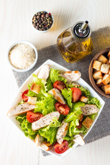 Fresh salad made of tomato, ruccola, chicken breast, eggs, arugula, crackers and spices. Caesar salad in a white, transparent bowl on wooden background