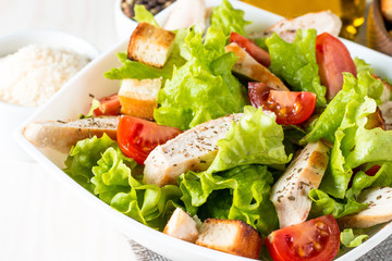 Fresh salad made of tomato, ruccola, chicken breast, eggs, arugula, crackers and spices. Caesar salad in a white, transparent bowl on wooden background