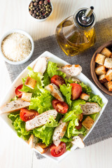 Fresh salad made of tomato, ruccola, chicken breast, eggs, arugula, crackers and spices. Caesar salad in a white, transparent bowl on wooden background