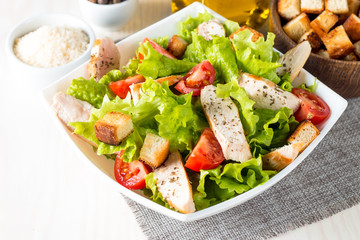 Fresh salad made of tomato, ruccola, chicken breast, eggs, arugula, crackers and spices. Caesar salad in a white, transparent bowl on wooden background