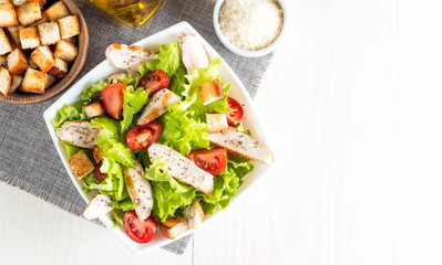 Fresh salad made of tomato, ruccola, chicken breast, eggs, arugula, crackers and spices. Caesar salad in a white, transparent bowl on wooden background