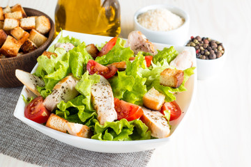 Fresh salad made of tomato, ruccola, chicken breast, eggs, arugula, crackers and spices. Caesar salad in a white, transparent bowl on wooden background