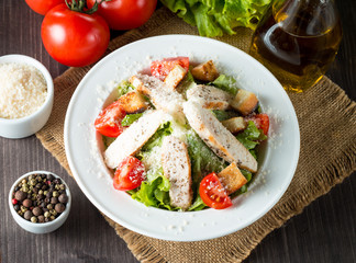 Fresh salad made of tomato, ruccola, chicken breast, eggs, arugula, crackers and spices. Caesar salad in a white, transparent bowl on wooden background